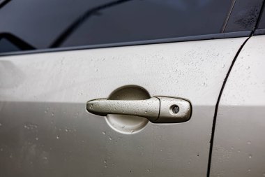 Fenerinde yağmur damlacıkları olan parlak gümüş renkli bir araba, parlak ışıklandırılmış bir oto yıkama istasyonuna yakın plan çekimde yakalandı.