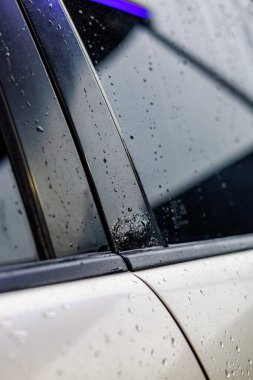 Kapalı araba gövdesi hasarı: ön taraftaki boya parçaları, arka tampondaki derin çizikler, ve yağmurlu koşullarda arka pencere direğinin yanındaki deformasyon.