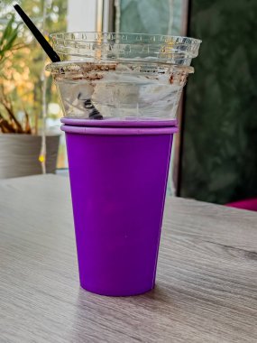 Tahta Masa üzerinde tek kullanımlık mor kahve fincanı. Ilık sarı Bokeh Işıkları Arkaplan, Kafenin iç kısmı yakın plan.