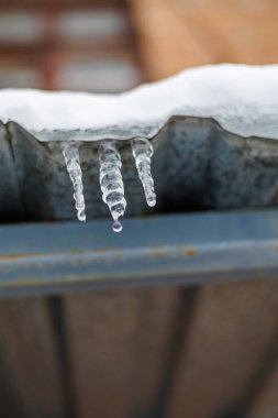 Parlak bir Kış Güneşi ve Mavi Gök 'e Karşı Bir Çatıda Asılı Tek Donmuş Buz Sarkıtı, Eriyen Buz ve Mevsimsel Hava Konsepti