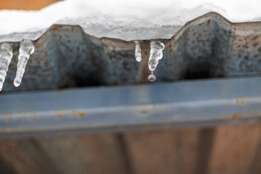 Parlak bir Kış Güneşi ve Mavi Gök 'e Karşı Bir Çatıda Asılı Tek Donmuş Buz Sarkıtı, Eriyen Buz ve Mevsimsel Hava Konsepti