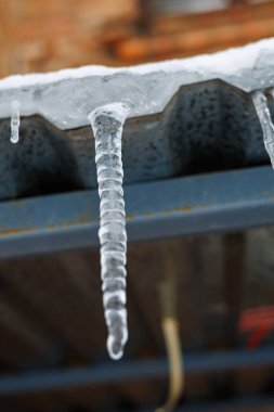 Parlak bir Kış Güneşi ve Mavi Gök 'e Karşı Bir Çatıda Asılı Tek Donmuş Buz Sarkıtı, Eriyen Buz ve Mevsimsel Hava Konsepti