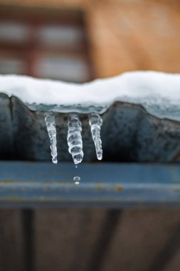 Parlak bir Kış Güneşi ve Mavi Gök 'e Karşı Bir Çatıda Asılı Tek Donmuş Buz Sarkıtı, Eriyen Buz ve Mevsimsel Hava Konsepti