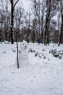 Karla kaplı bir şehir parkında tahta sopa tutan yalnız bir kardan adam: kış aktiviteleri ve çocukluk yaratıcılığı kavramı.