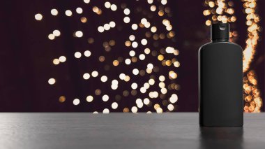 En az siyah kozmetik şişesi arka planda sıcak altın bokeh ışıkları ile karanlık bir yüzeyde duruyor. Lüks cilt bakımı ya da güzellik ürünü reklamı için mükemmel..
