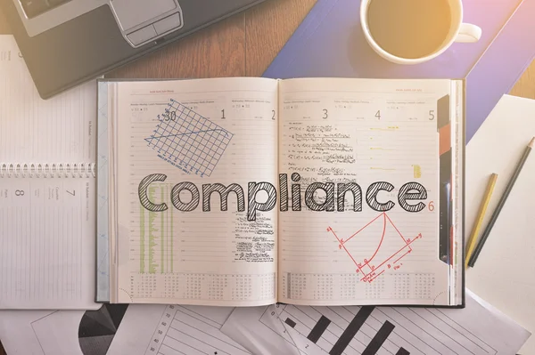 Notitieboekje met tekst in Compliance op tafel met koffie en sommige diagrammen — Stockfoto
