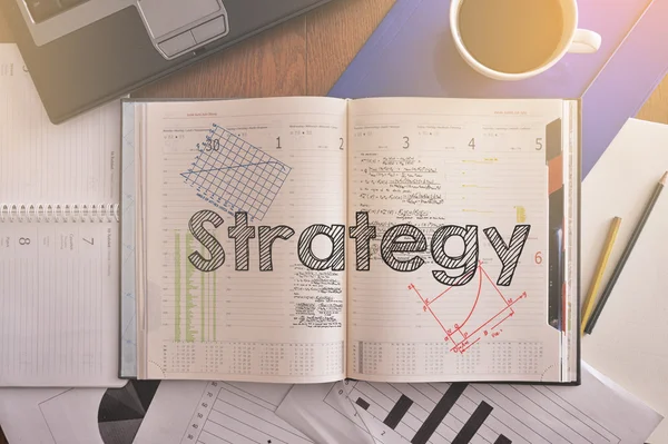 Cuaderno con texto dentro Estrategia sobre mesa con café y algunos diagramas — Foto de Stock