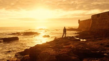 İspanya, Endülüs 'ün Cadiz kıyısında gün batımında Castillo de San Sebastian' ın üzerine altın bir parıltı saçıyor.