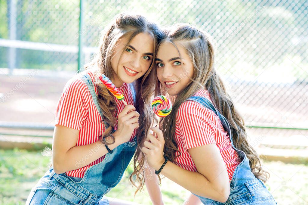 Portrait of two beautiful girls twins with lollipop caramel