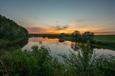 Sakin bir yaz günbatımı, ağaçları yansıtan sessiz bir nehrin üzerinde.