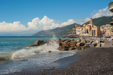 Balıkçı kasabası Camogli kıyıları, renkli evler ve bir kale, kayalara vuran dalgalar
