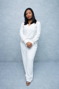 Beyaz elbiseli göz kamaştırıcı siyahi kadın, ciddi bir ifadeyle kameraya bakıyor. Tam boy fotokopi stüdyosu, kendine güven, iş kadını ve kadın kariyer sorunları için mükemmel..