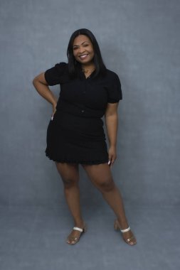 Siyah elbiseli çekici Brezilyalı kadın zarif bir şekilde poz veriyor ve kameraya gülümsüyor. Fotokopi alanı olan bir stüdyo resmi, özgüven, kendine güven ve kadın güzellik kavramları için ideal..