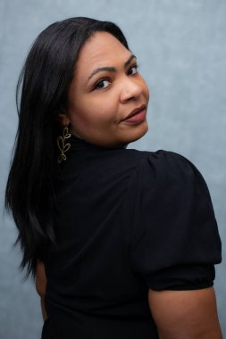 Güzel ve iri yapılı kahverengi tenli bir kadın omzunun üstünden bakıyor. Belden yukarı, vücut pozitifliği, bireysellik, çeşitli güzellik ve kadınsı kendine güven kavramları için ideal..