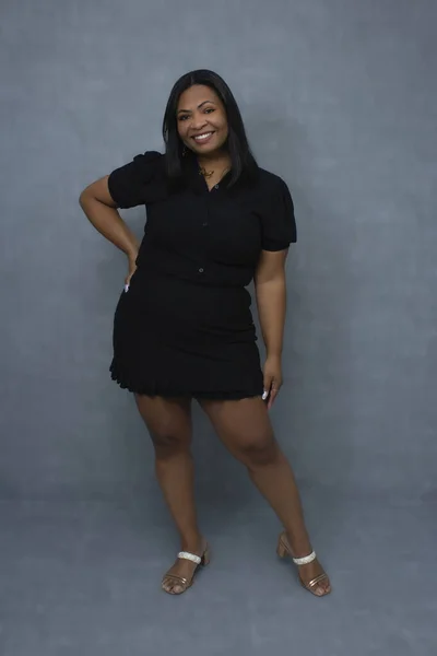 Siyah elbiseli çekici Brezilyalı kadın zarif bir şekilde poz veriyor ve kameraya gülümsüyor. Fotokopi alanı olan bir stüdyo resmi, özgüven, kendine güven ve kadın güzellik kavramları için ideal..