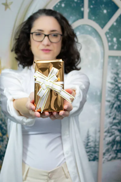 Kameraya doğru uzanmış kollarıyla Noel hediyesi sunan bir kadın. Stüdyo portresi Noel hediyeleri, tatil kutlamaları ve kış mevsimi promosyonları için mükemmel..