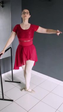 Balerin barın yanında battement tendu jeti yapıyor. Dikey video dans dersleri, bale dersleri, sosyal medya dans dersleri ve acemi dansçı eğitimi için harika..