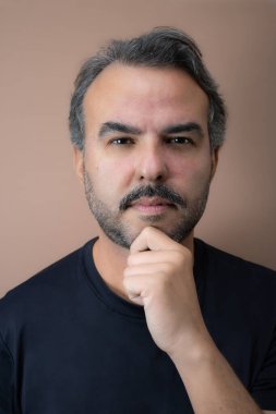 Gri saçlı, gri sakallı, elleri çenesinde poz veren orta yaşlı bir adamın vesikalığı. Erkek konuları, planlama ve düşünme konuları ve problem çözme içeriği için dikey stüdyo portresi ideal.