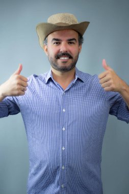Neşeli kovboy gülümsüyor ve baş parmağını kaldırıyor. Tarafsız arka plan ile belden yukarı çekim, mutluluk ve olumlu duygu temaları, çiftçi içeriği ve tarım konuları için harika.