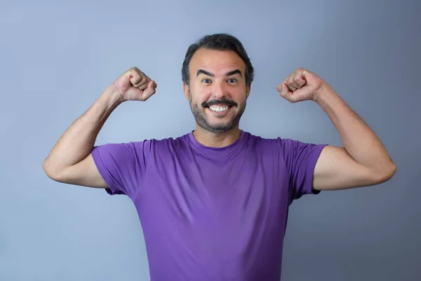 Yumrukları havada, mor tişört giymiş, zaferi kutlayan neşeli bir adam. Kopya alanı ile belden yukarı yatay çekim, spor yarışması, başarı ve aktif yaşam tarzı temaları için ideal.