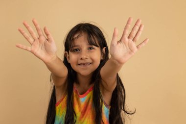 Çok renkli tişörtlü gülümseyen kız avuçlarını neşeli bir hareketle açıyor. Kopya alanı olan açık kahverengi arkaplan, tasarım veya reklam için ideal