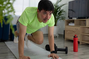 Adamın biri oturma odasındaki bir paspasın önünde dağ tırmanışçısı egzersizi yapıyor. Ev çalışması, kardiyo, enerji ve sağlıklı yaşam tarzı.