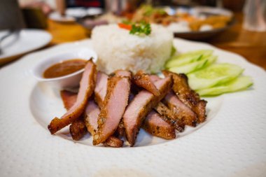 Buharda pilavın üstünde ızgara domuz eti ve beyaz tabakta sebze.