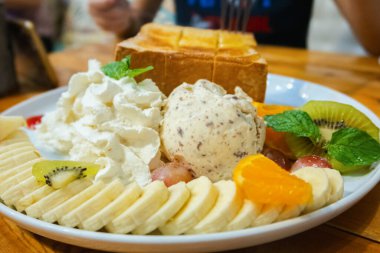 Krem şantili dondurma, muz dilimleri, çilek suyu ve bal ahşap masada bir fincanda.