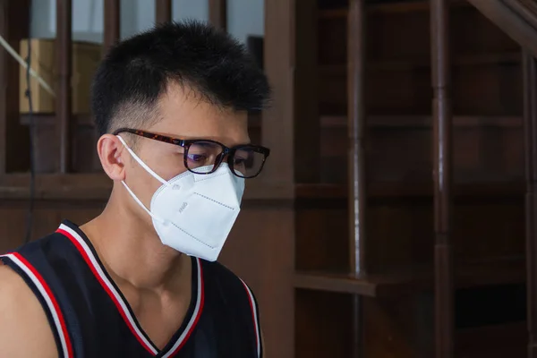 asian man wear basketball jersey with hygienic mask and sitting in house for protection