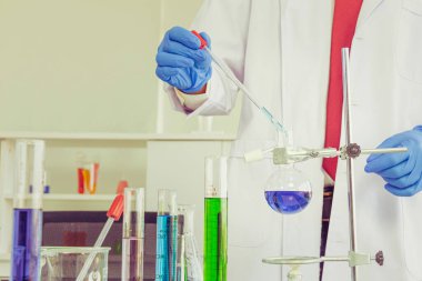 Erkek bilim adamı laboratuarda mavi eldiven giymiş kimyasal test tüpü üzerinde bir deney yapıyor.