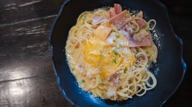 Carbonara soslu spagetti ve siyah tabakta jambon.