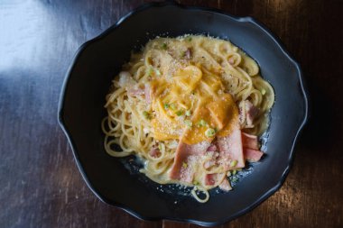 Carbonara soslu spagetti ve siyah tabakta jambon.