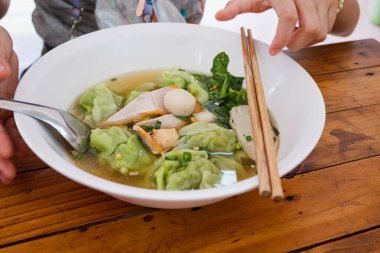 Yeşil tapyoka unlu domuz köftesi ve kırmızı domuz dilimi ve üzerine çubuklar konulmuş beyaz kasede sebze.