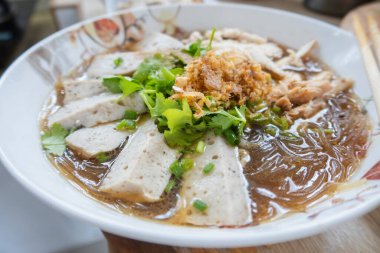 Sebzeli beyaz domuz sosisi ile kaynatılmış vermicelli; mutfakta yemek çubuklarıyla serpiştirilmiş bir kase.