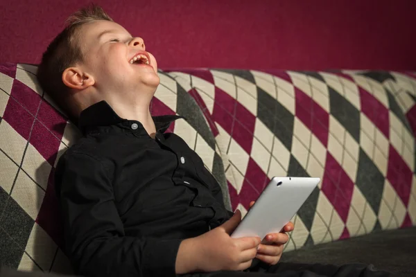 Niño en el salón en el sofá jugando en la tableta — Foto de Stock