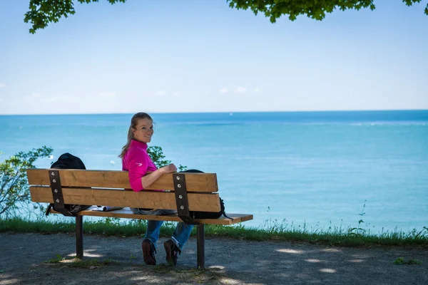 Jovem bela mulher sentada em um banco na margem do lago e w — Fotografia de Stock