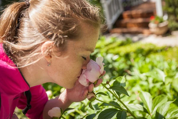 Young beautiful woman enjoying scent of a rose blooming in the g — Stock Photo, Image