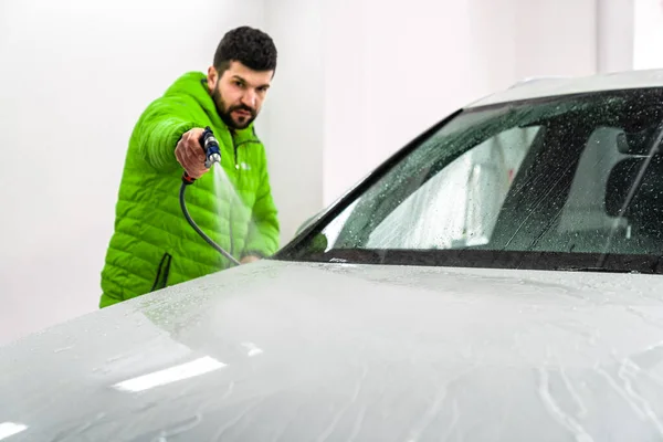 wash the car by spraying water from a high pressure hose with foam