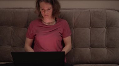 Kanepede dizüstü bilgisayarı olan genç bir kadın evde serbest çalışıyor.