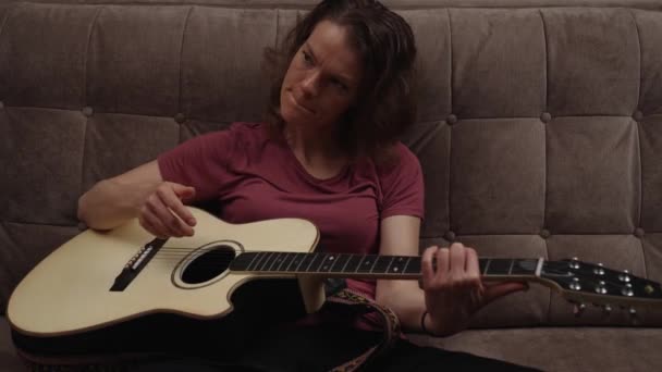 Домашние уроки гитары онлайн. женщина играет на гитаре дома на диване. — стоковое видео