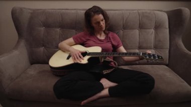 Kanepede gitar çalan bir kadın.