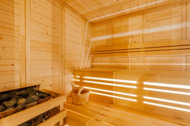 Modern bir sauna odasının içi sıcak ahşap banklar, taşlarla dolu bir metal ısıtıcı ve sağIık ve refah için rahatlatıcı bir ortam sağlayan ahşap bir kova.