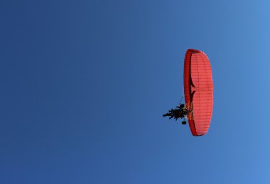 Mavi gökyüzünde uçan Yamaçparaşütü ve kırmızı Yamaçparaşütü bir motor ile bir yolcu.