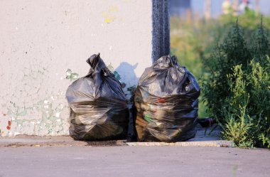 Otobüs durağının yanında iki siyah çöp torbası.