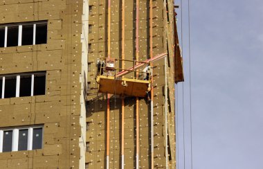 inşaat işçileri ile sarı beşik bir yeni inşa edilen yüksek katlı bina askıya.