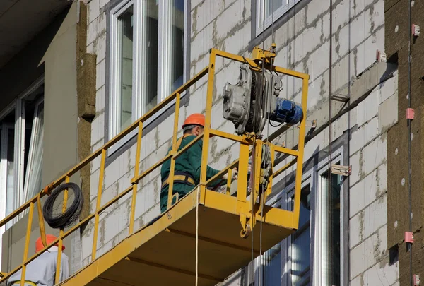 Berço amarelo suspenso da construção com trabalhadores em um edifício alto recentemente construído — Fotografia de Stock