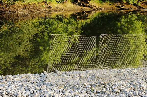 Malha protetora de metal perto do canal com água protege o derramamento de estradas de cascalho — Fotografia de Stock