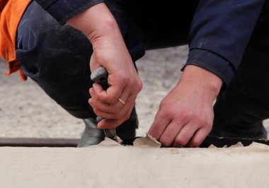 İşçiler suyu uzak tutmak için su yalıtımı için çatı malzemelerinin parçalarını kesiyorlar.