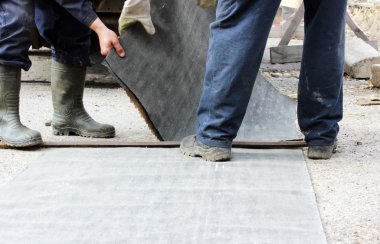 İşçiler suyu uzak tutmak için su yalıtımı için çatı malzemelerinin parçalarını kesiyorlar.