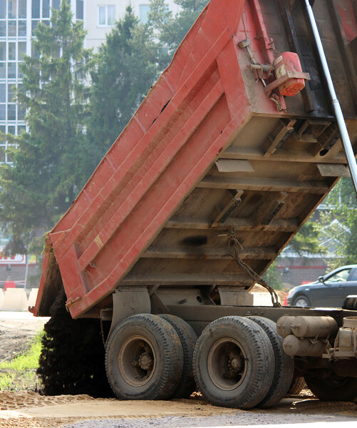 грузовик разгружает торф, вырытый при строительстве дороги из глубин земли
